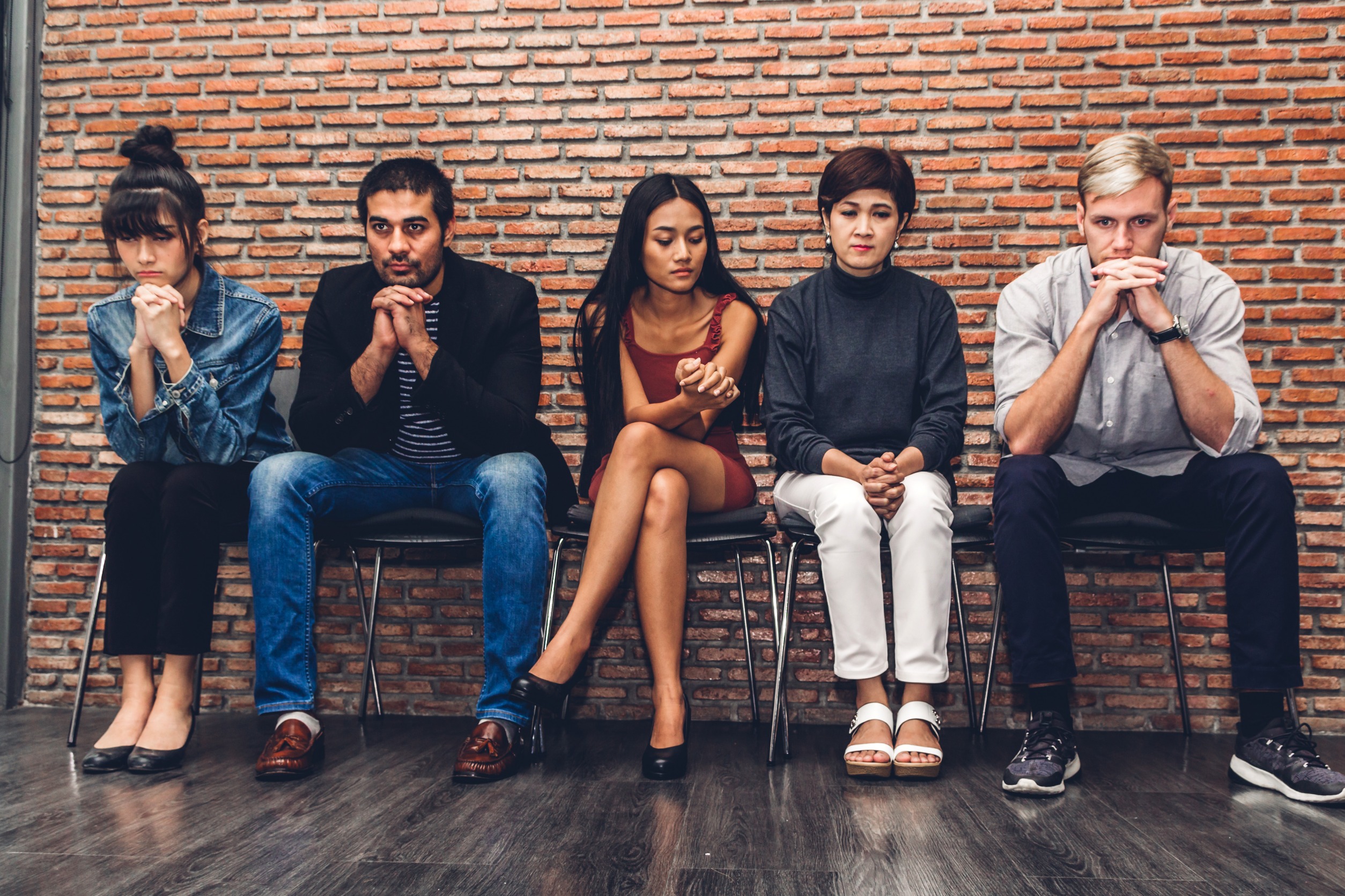cinco personas con cara de preocupacion sentadas con fondo de pared ladrillo