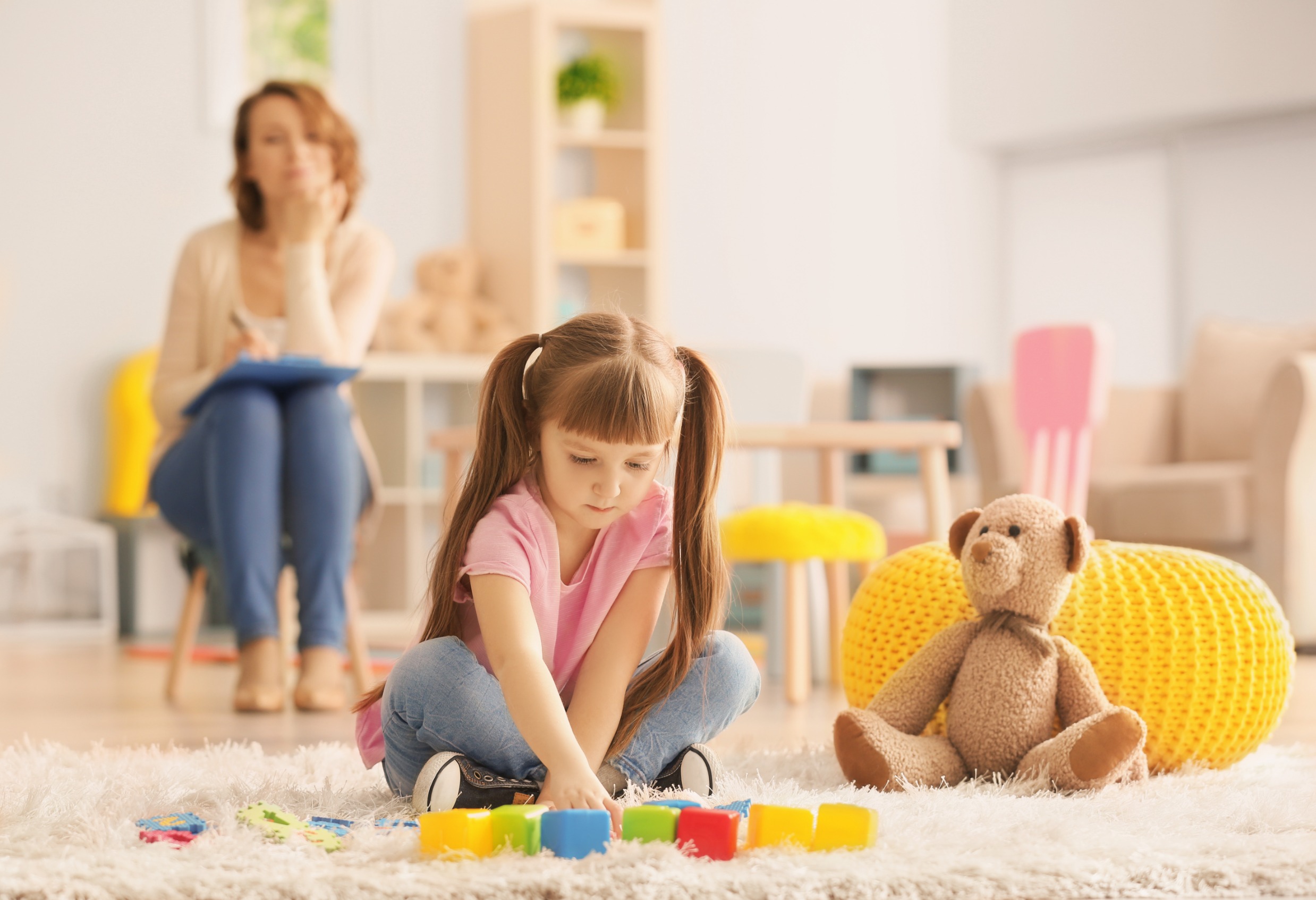niña juega con psicologa observandola al fondo